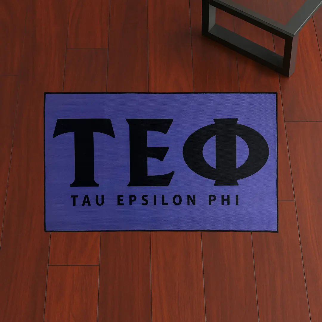 Custom Rug – Tau Epsilon Phi Letters Purple & Black custom rug by Sirenicate Rugs, prominently displayed on a vibrant dark hardwood floor background.