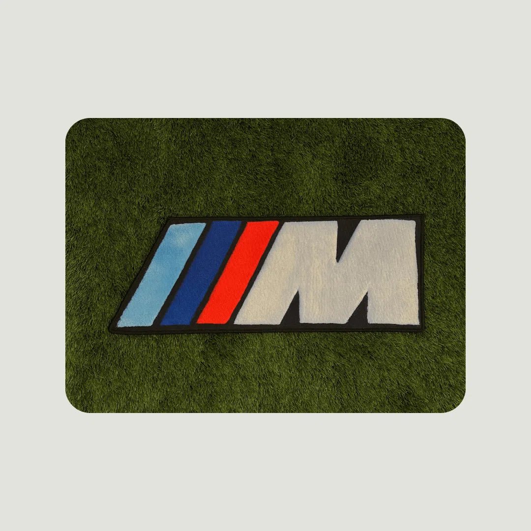 Multiple Sport M Logo Rugs displayed on turf in different sizes to show scale, layout options, and bold contrast.